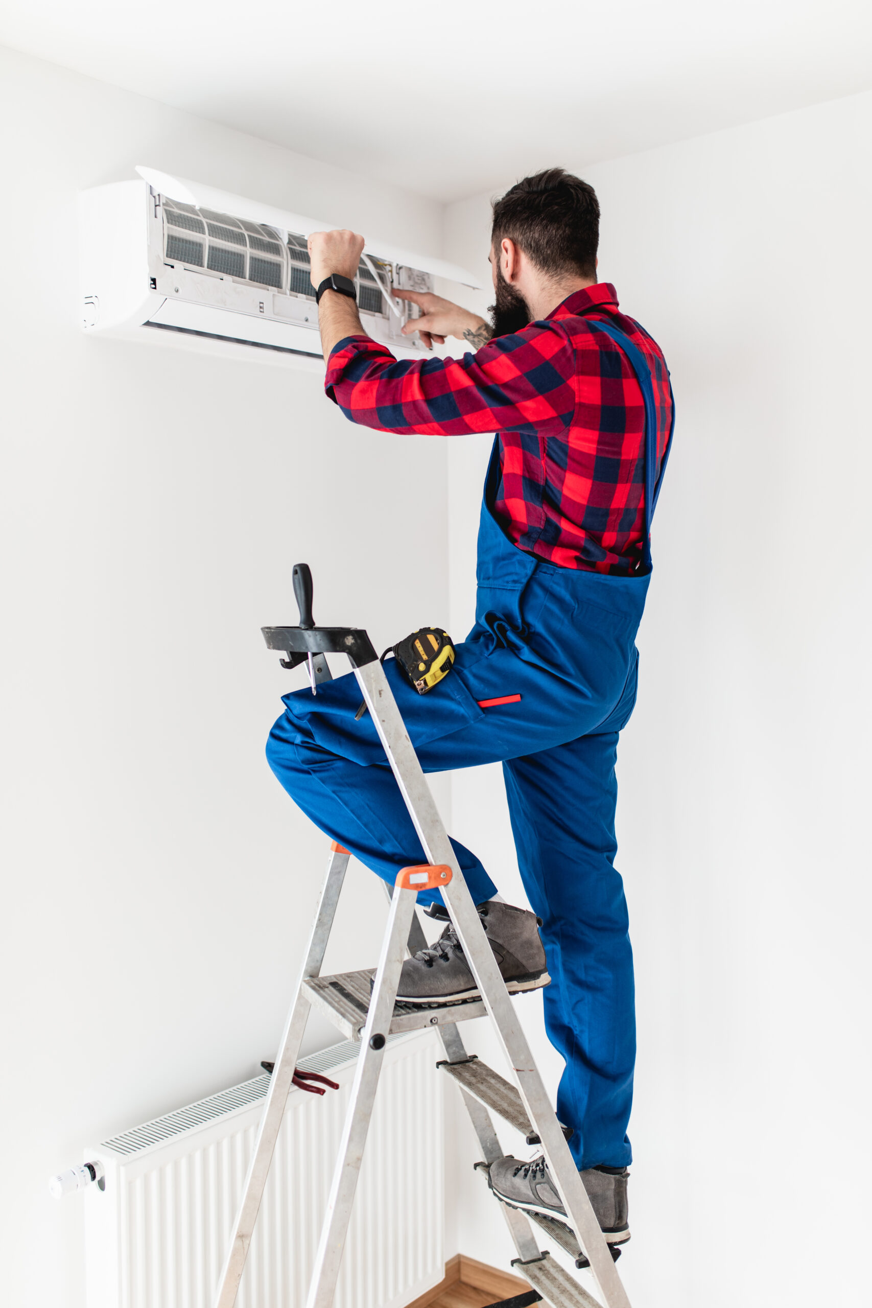 Young bearded handyman repairing air conditioner.